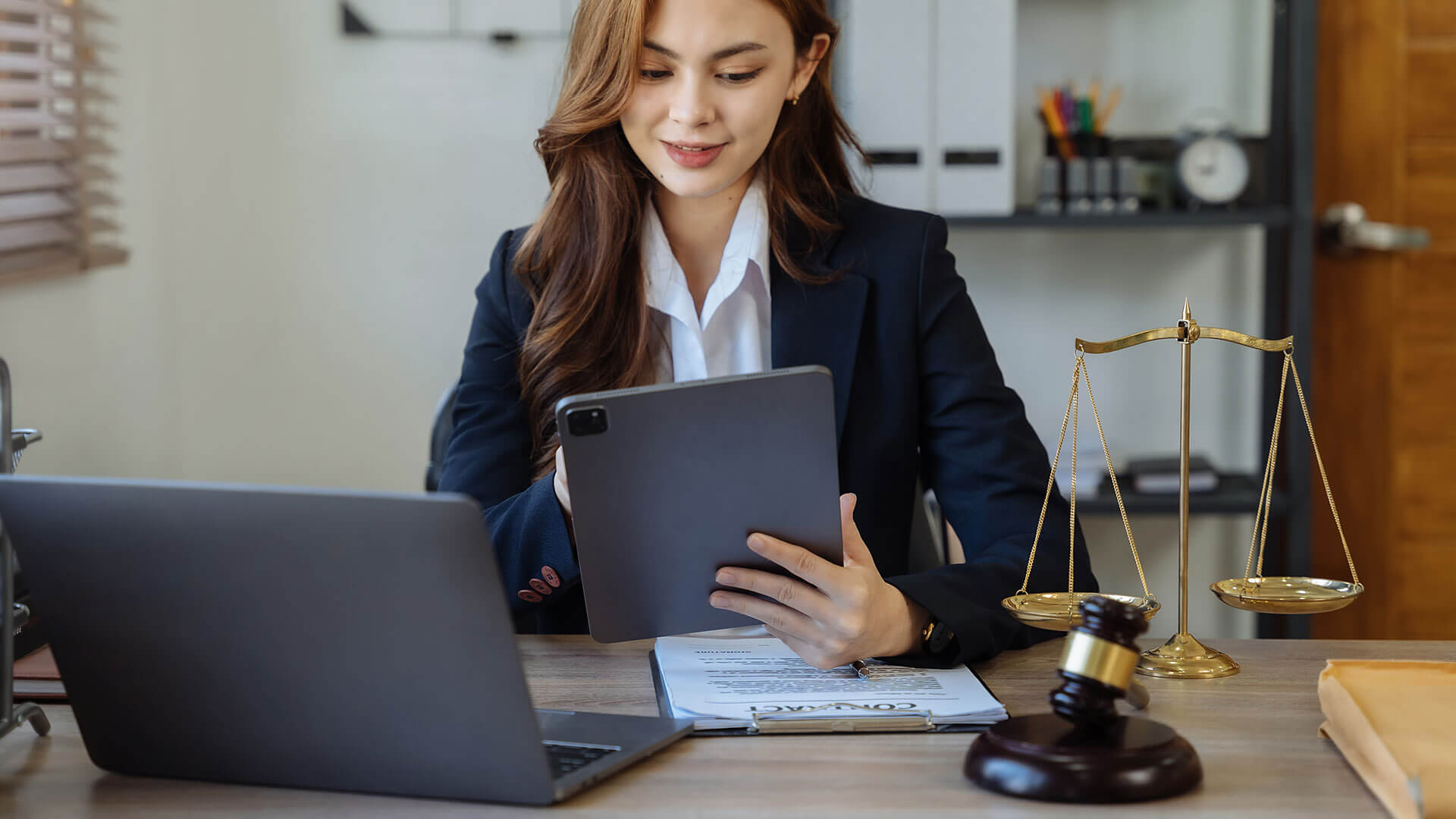 Female lawyer looking at iPad with laptop on desk in front of her